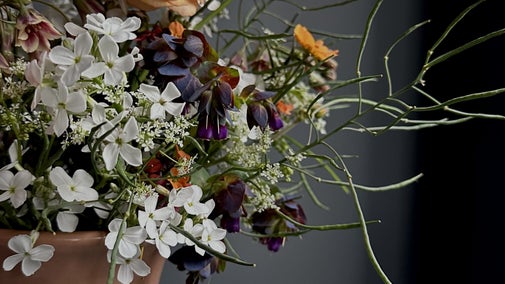 A multicoloured floral arrangement with foliage in a peach coloured ceramic bowl